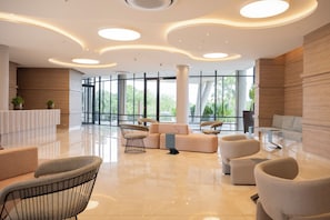 A spacious lobby with a modern design, featuring a reception desk, seating area with sofas and chairs, and large windows offering a view of greenery outside. - Morros Park. Exclusive Beach & Nature Retreat (Bolívar)