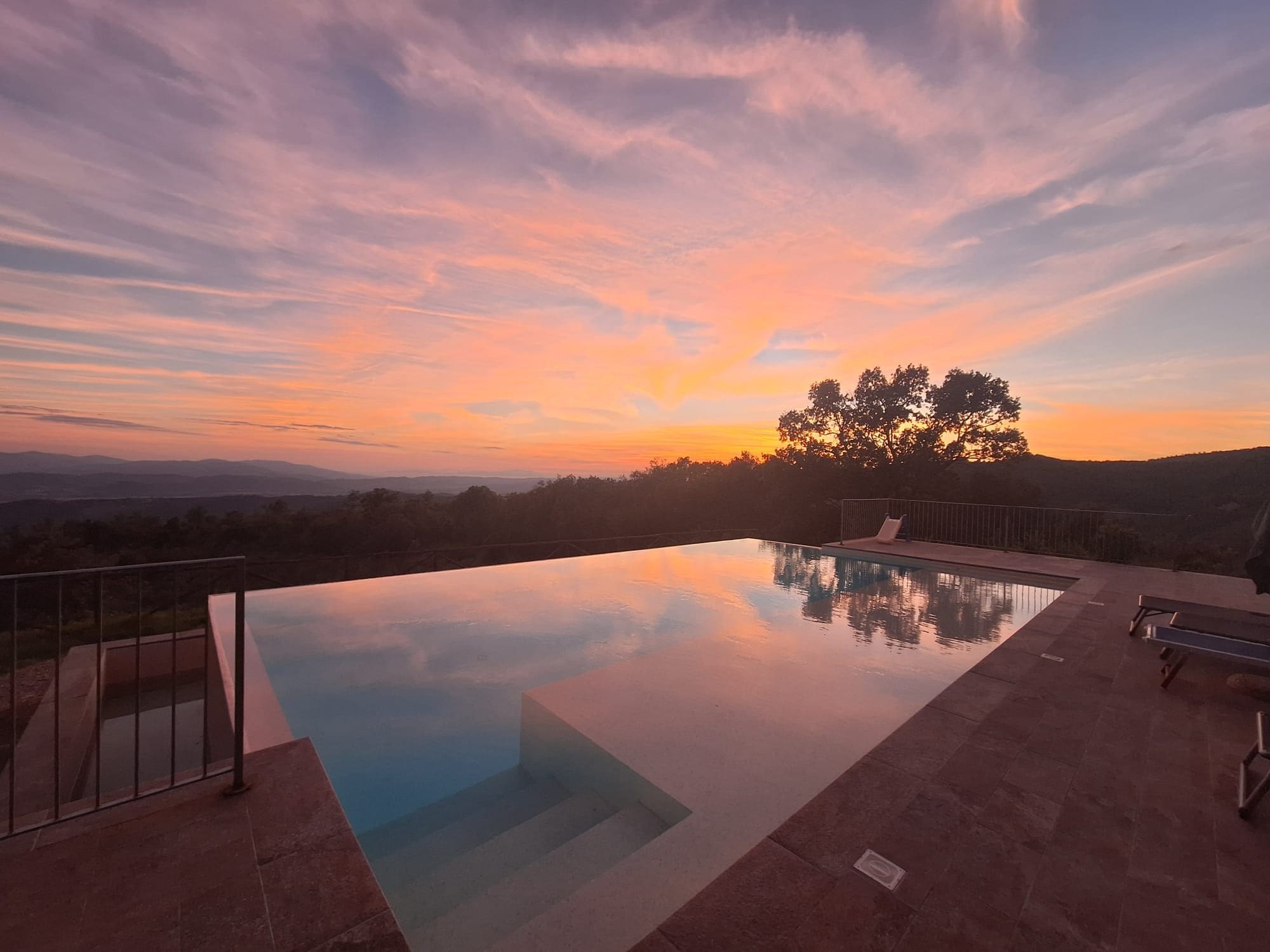 An infinity pool with a clear view of the sunset and distant hills.