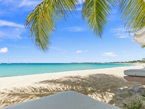Uma praia com areia branca, águas turquesa cristalinas e alguns veleiros ao longe.