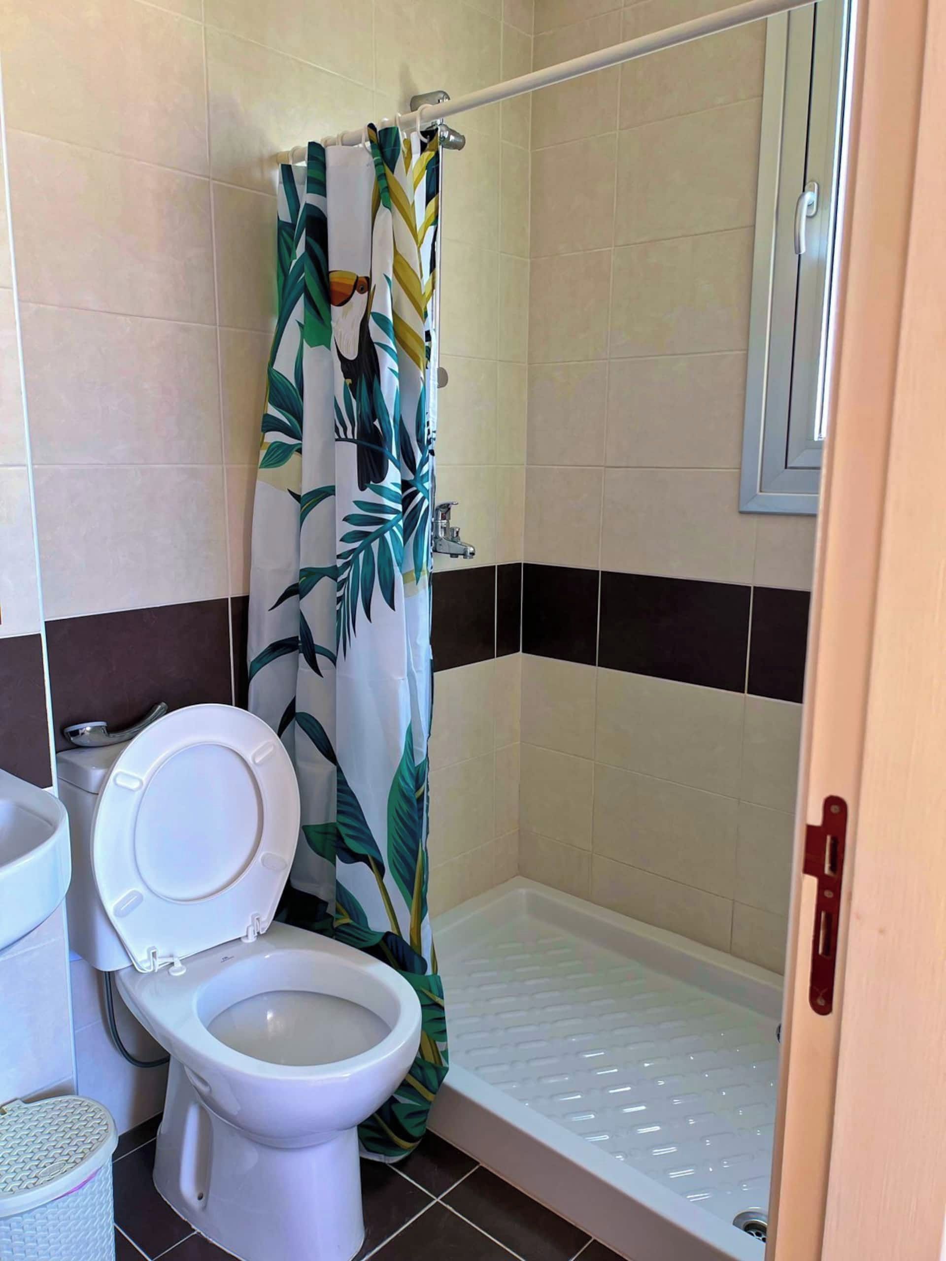 A bathroom with a toilet, a shower with a patterned curtain, and tiled walls.