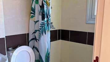 A bathroom with a toilet, a shower with a patterned curtain, and tiled walls.