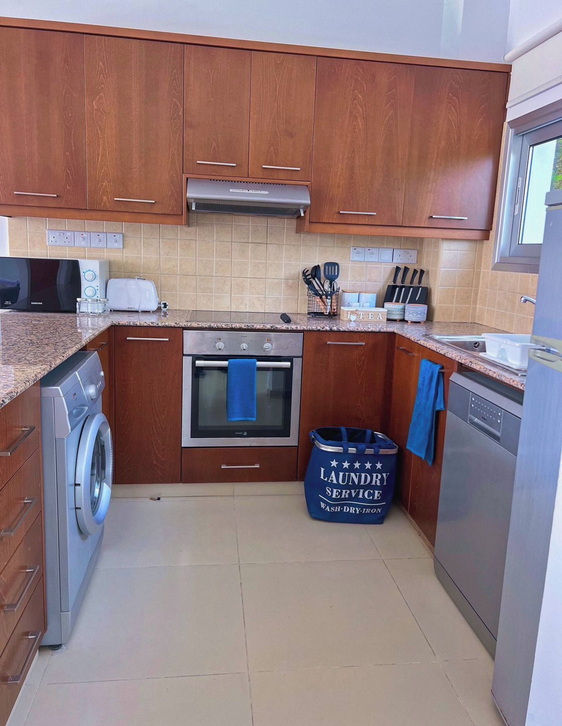 A kitchen with wooden cabinets, a stainless steel oven, a washing machine, and a dishwasher.