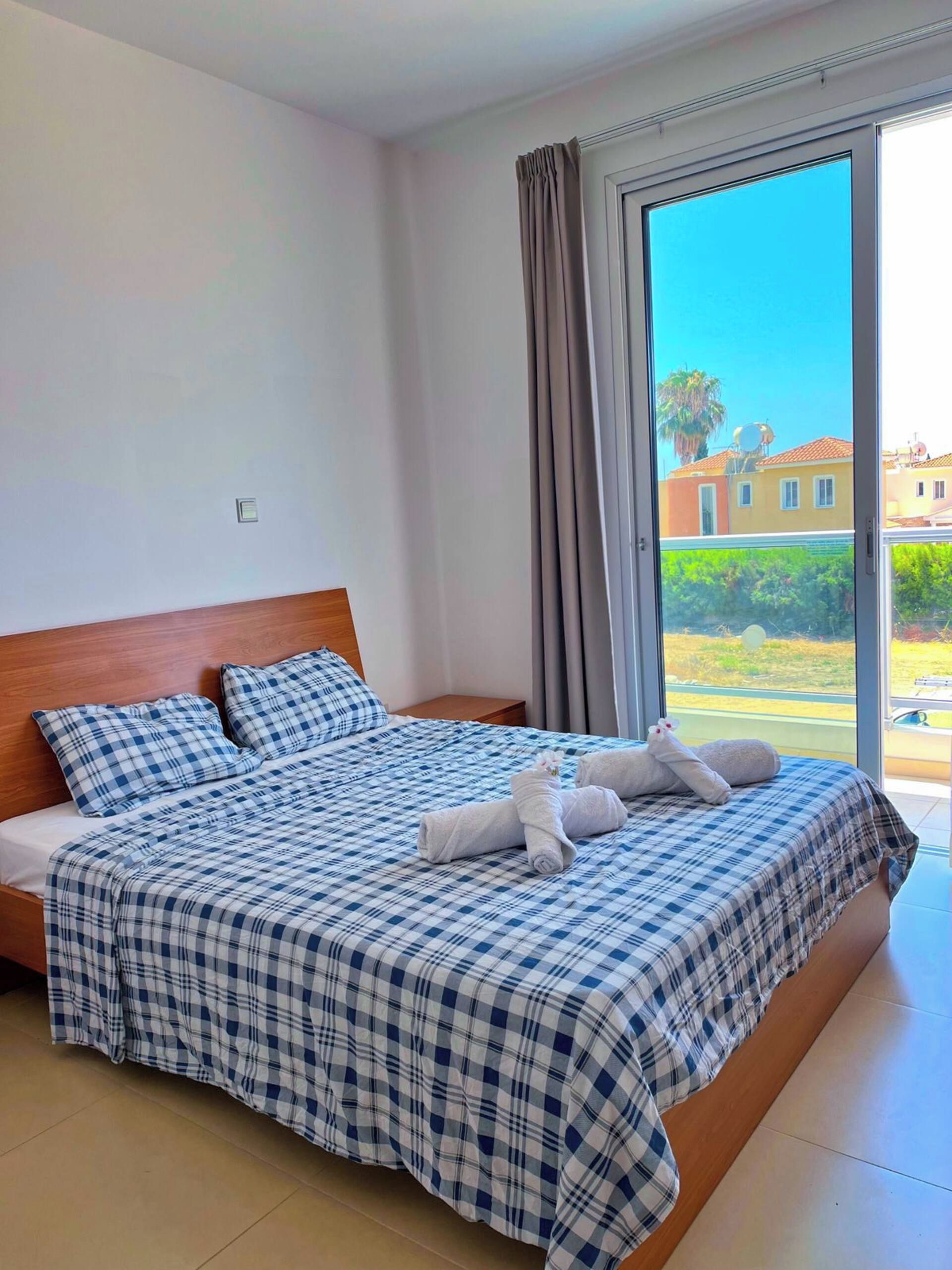 A hotel room with a large bed, a wooden headboard, a view through a sliding glass door, and a small table.