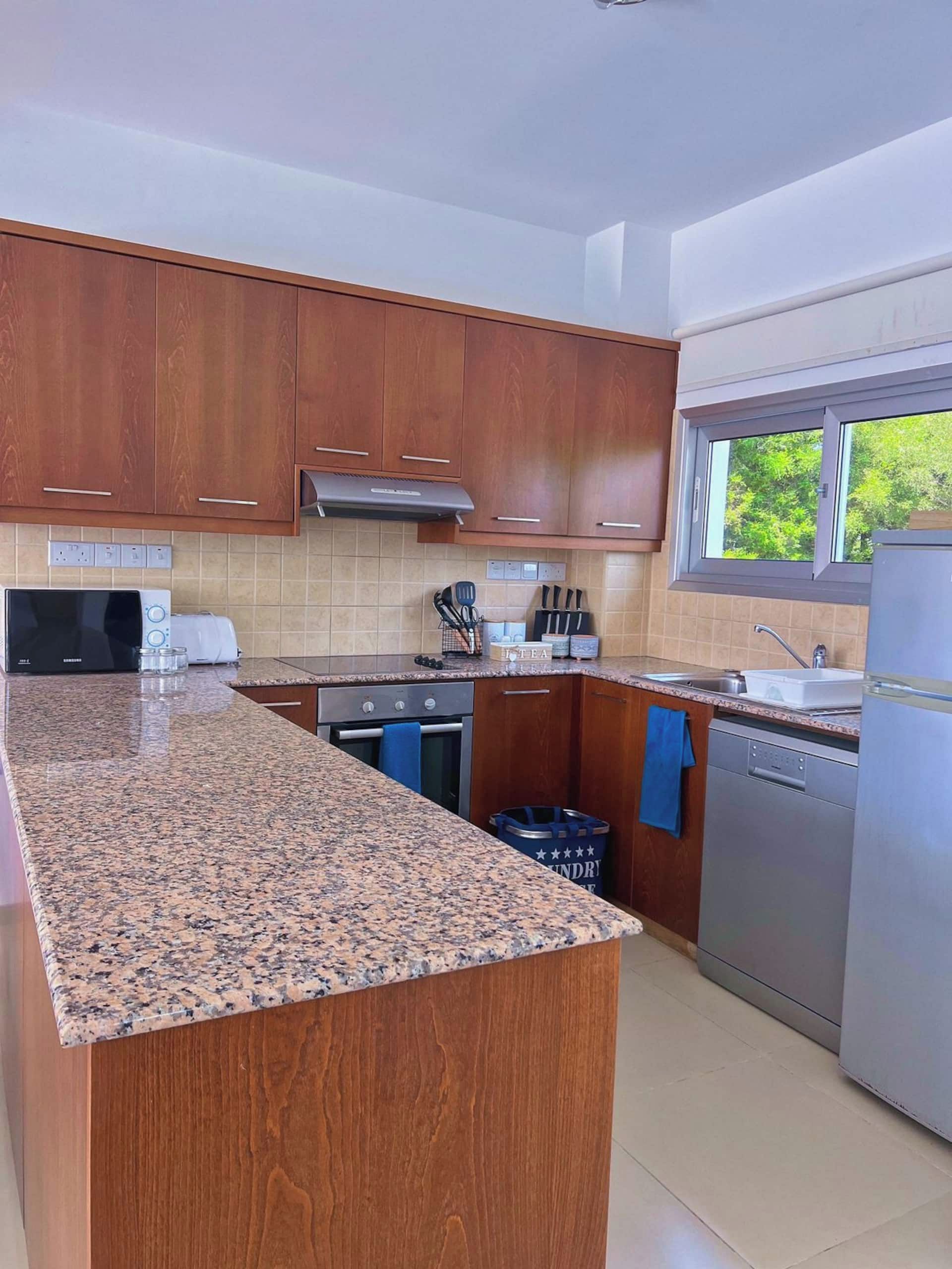 A modern kitchen with wooden cabinets, granite countertops, stainless steel appliances, and a window providing natural light.