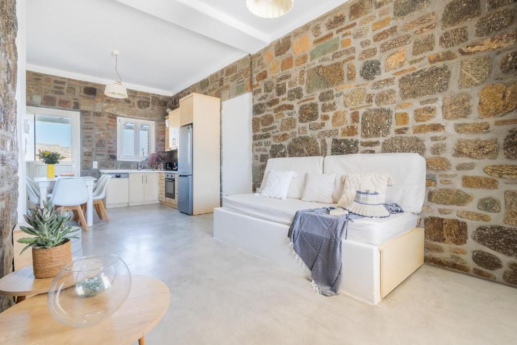A modern living space with a stone wall, a white sofa, a dining area with a table and chairs, and a kitchen in the background.