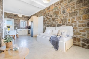 Un espacio habitable moderno con una pared de piedra, un sofá blanco, un área de comedor con mesa y sillas, y una cocina al fondo.