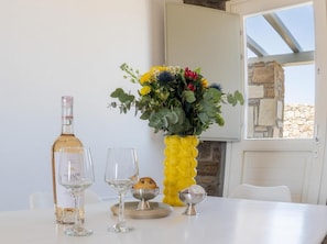 Una mesa con una botella de vino, dos copas, un cuenco de pan y un jarrón amarillo con flores.