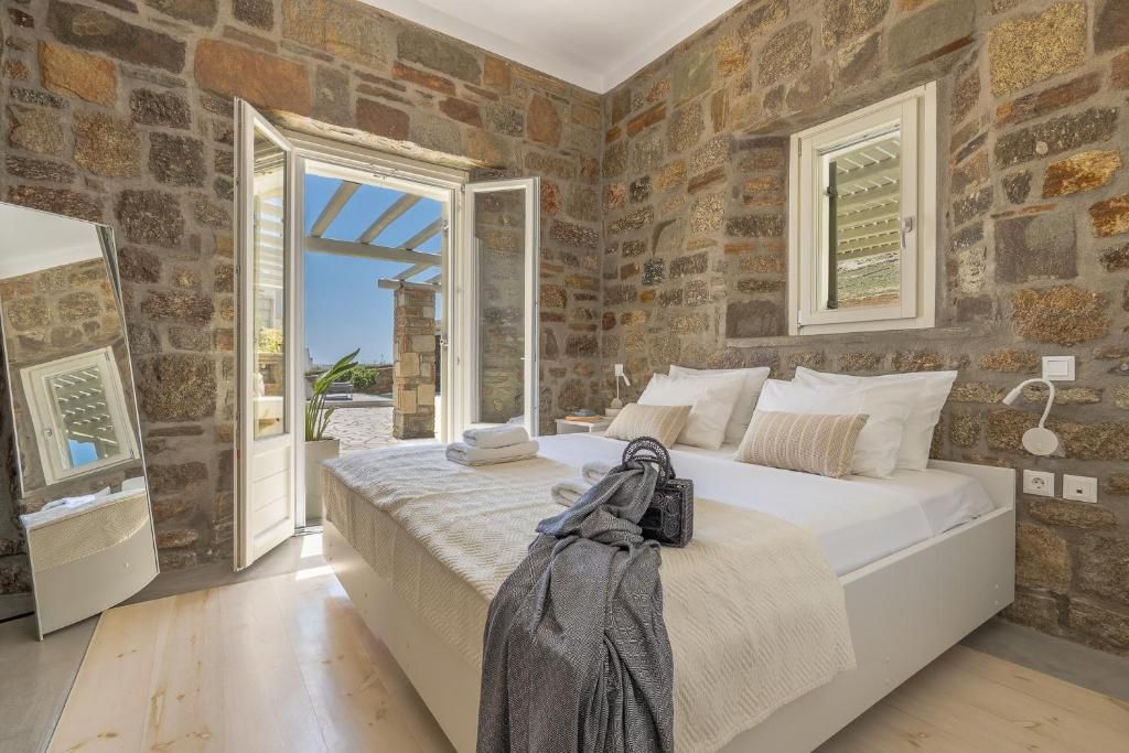 A bedroom with stone walls, a large bed, a window, and a door leading outside.