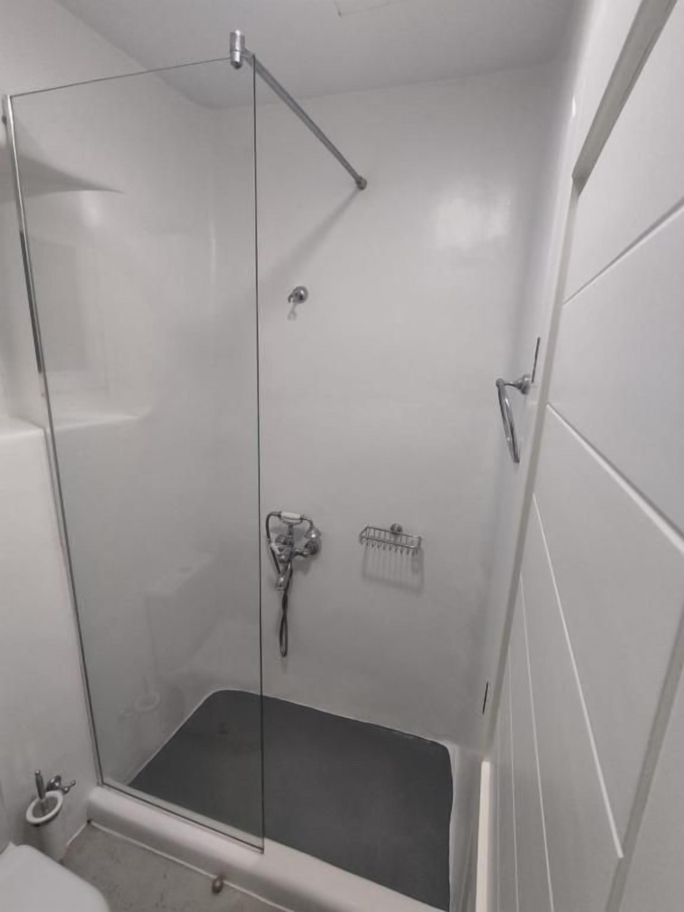 Ducha con mampara de vidrio, cabezal de ducha manual, un estante pequeño y pared de azulejos.
