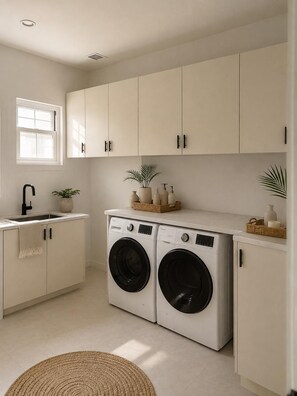A laundry room with two front-loading washing machines, a sink, and cabinets. - Luxurious 6 bed, 7 bath estate in Fitches Creek for large families and groups (Fitches Creek)