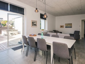 A modern dining area with a white table and grey chairs, a glass door leading outside, and a ceiling with exposed beams. - 4 Star Holiday Home in Ebeltoft (Ebeltoft)