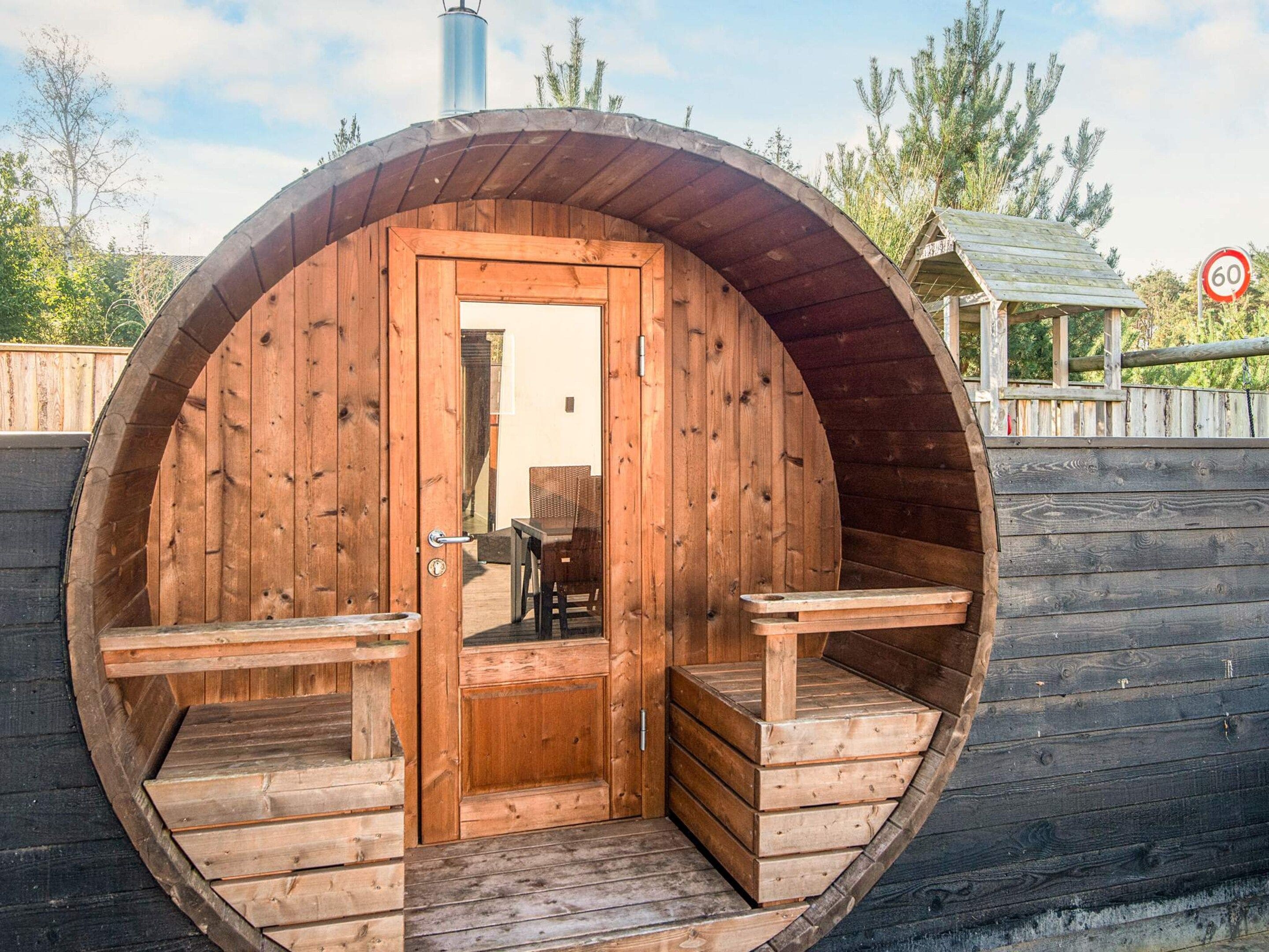 A wooden barrel-shaped structure with a door, two benches, and a table inside.