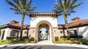 A gated entrance with a stone archway, palm trees, and a clear blue sky. - 4BR Townhome Solterra Resort Lazy River & Pool (Davenport)