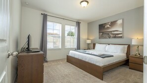 Ein Schlafzimmer mit einem Einzelbett, einem Nachttisch, einer Lampe, einem Bild an der Wand und einem Fenster mit Vorhängen.