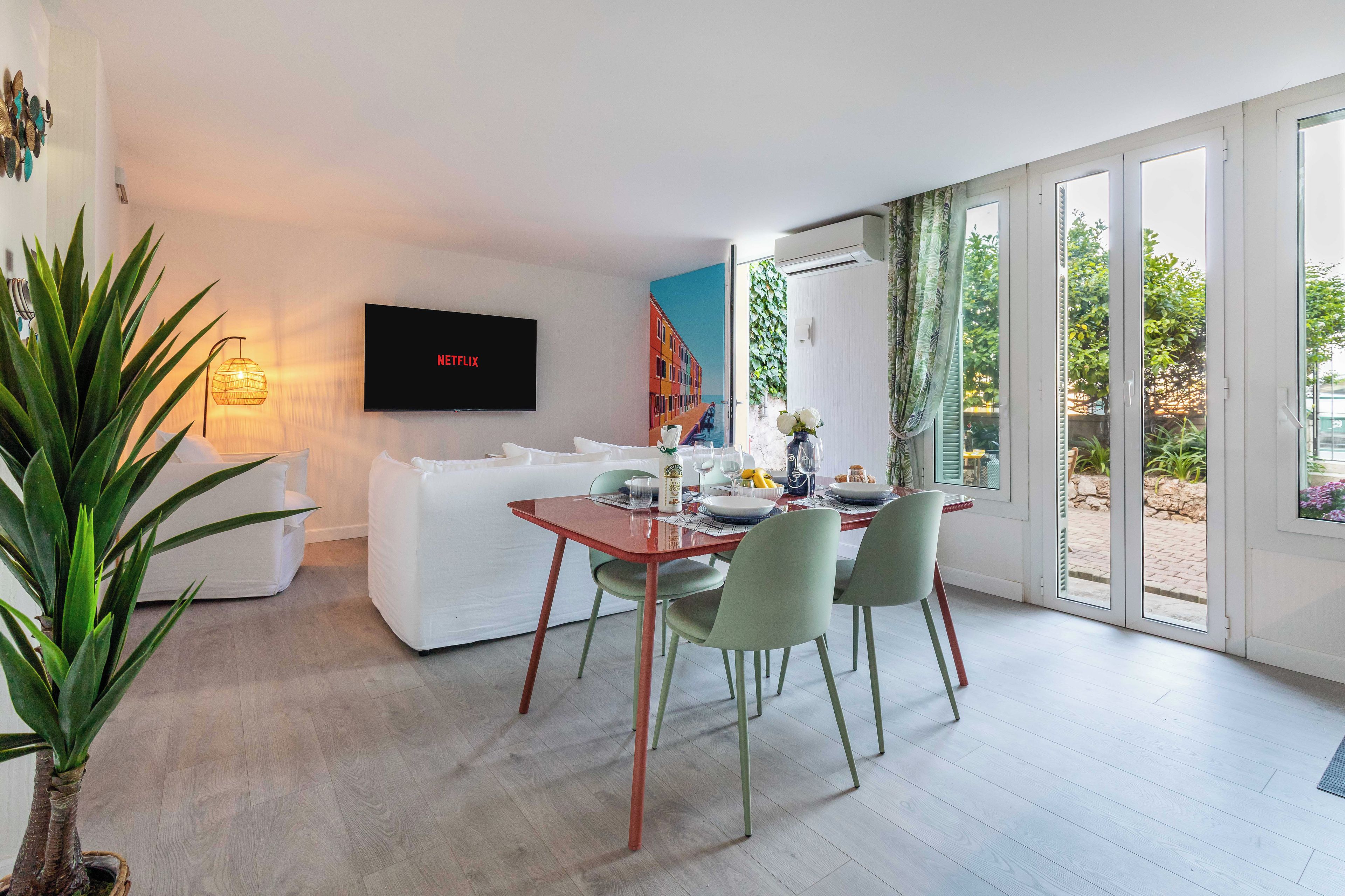 Uma sala de estar moderna com área de jantar, TV de tela plana na parede e uma grande janela com vista para o exterior.