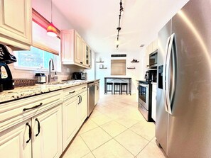 A modern kitchen with white cabinets, a stainless steel refrigerator, and a tiled floor. - Sarasota 4BR Home Near Siesta Key • Fenced Yard, Fire Pit & Pets (Sarasota)