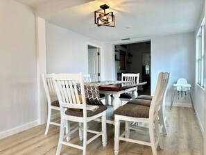 Een eetruimte met een witte tafel en stoelen, een tafelkleed met een patroon en een moderne lamp.