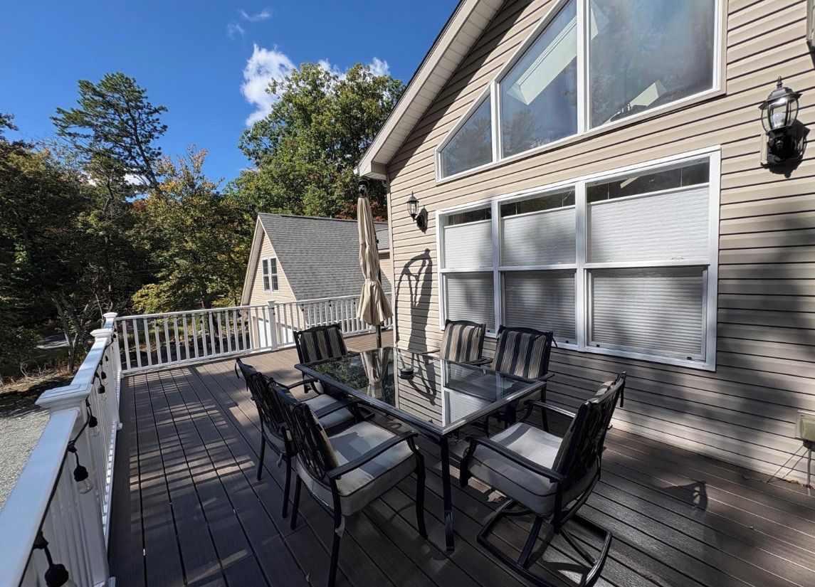 A deck with a glass-top table and chairs, a white railing, and a garage door.