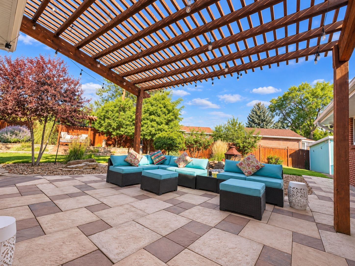 A covered patio area with a wooden pergola, outdoor furniture, and a stone-tiled floor.