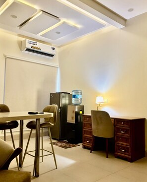 Habitación de hotel con comedor, dispensador de agua, escritorio y lámpara.