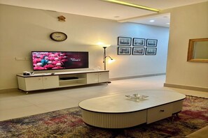Ein modernes Wohnzimmer mit Flachbildfernseher, einer weißen Unterhaltungsanlage, einem runden Couchtisch und einem gemusterten Teppich.