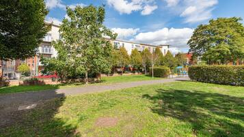 Ein Park mit einem gepflasterten Weg, Bäumen und Wohnhäusern im Hintergrund.