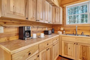 A kitchen with wooden cabinets, a coffee maker, a toaster, and a window with a view of trees. - The Outpost, 5 minutes to Old Man's Cave, Sleeps 10, Hot Tub, Fire Pit. (Logan)
