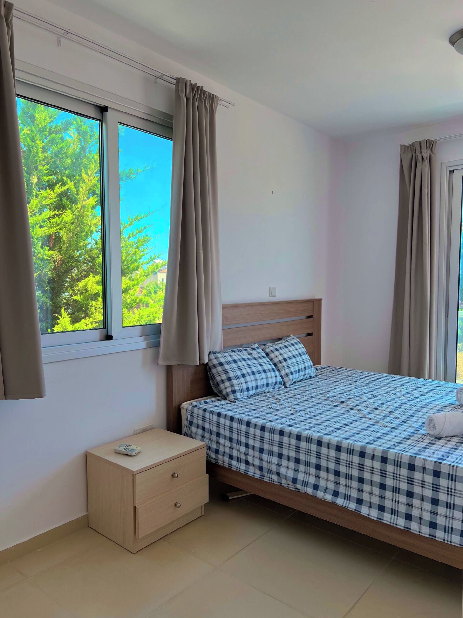 A bedroom with a bed, a nightstand, and a window with curtains.