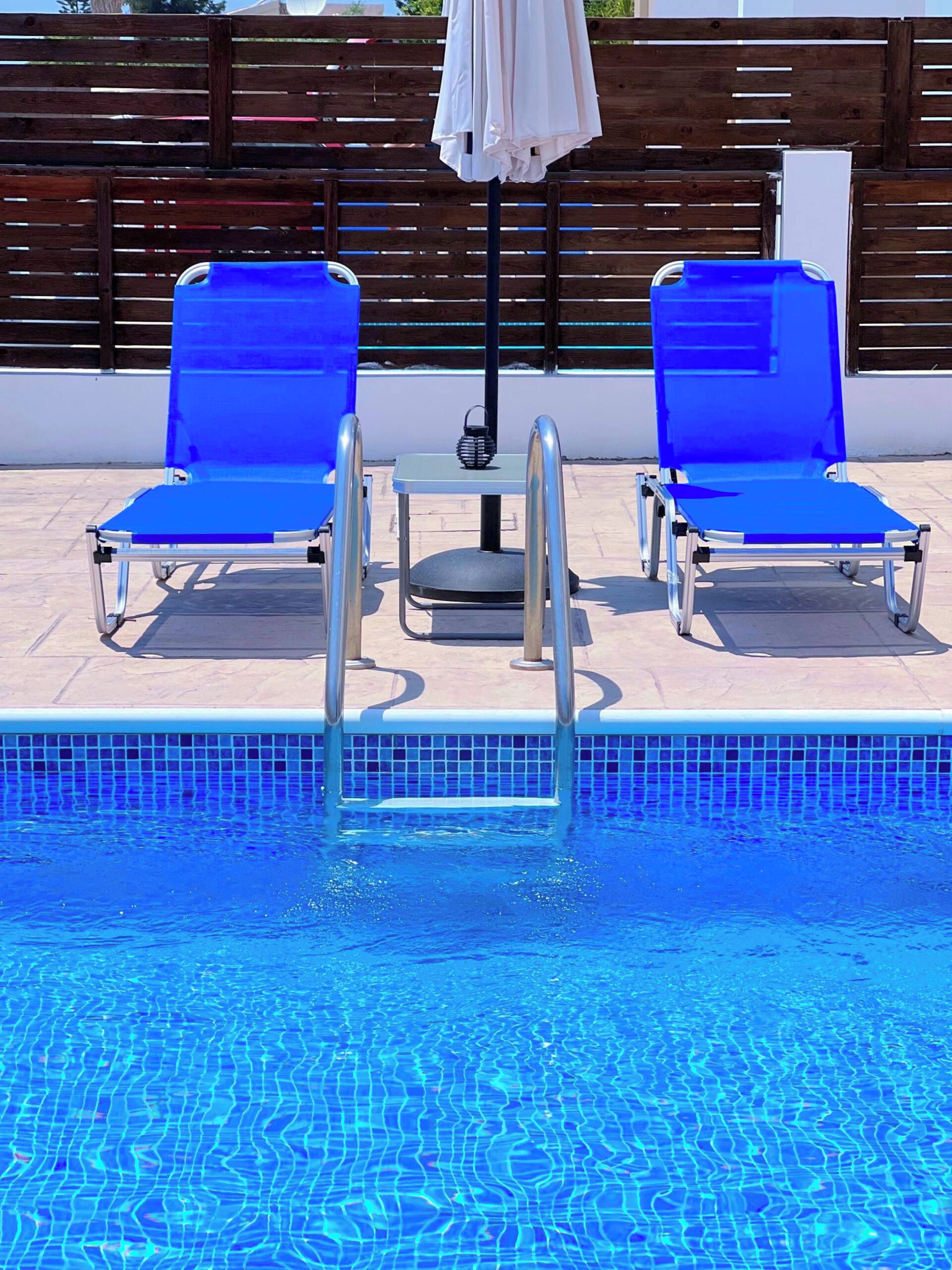 A swimming pool with two blue lounge chairs and a small table with a white umbrella.