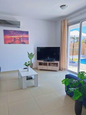 Un saló modern amb una televisió plana, una taula de cafè blanca i una planta en test.