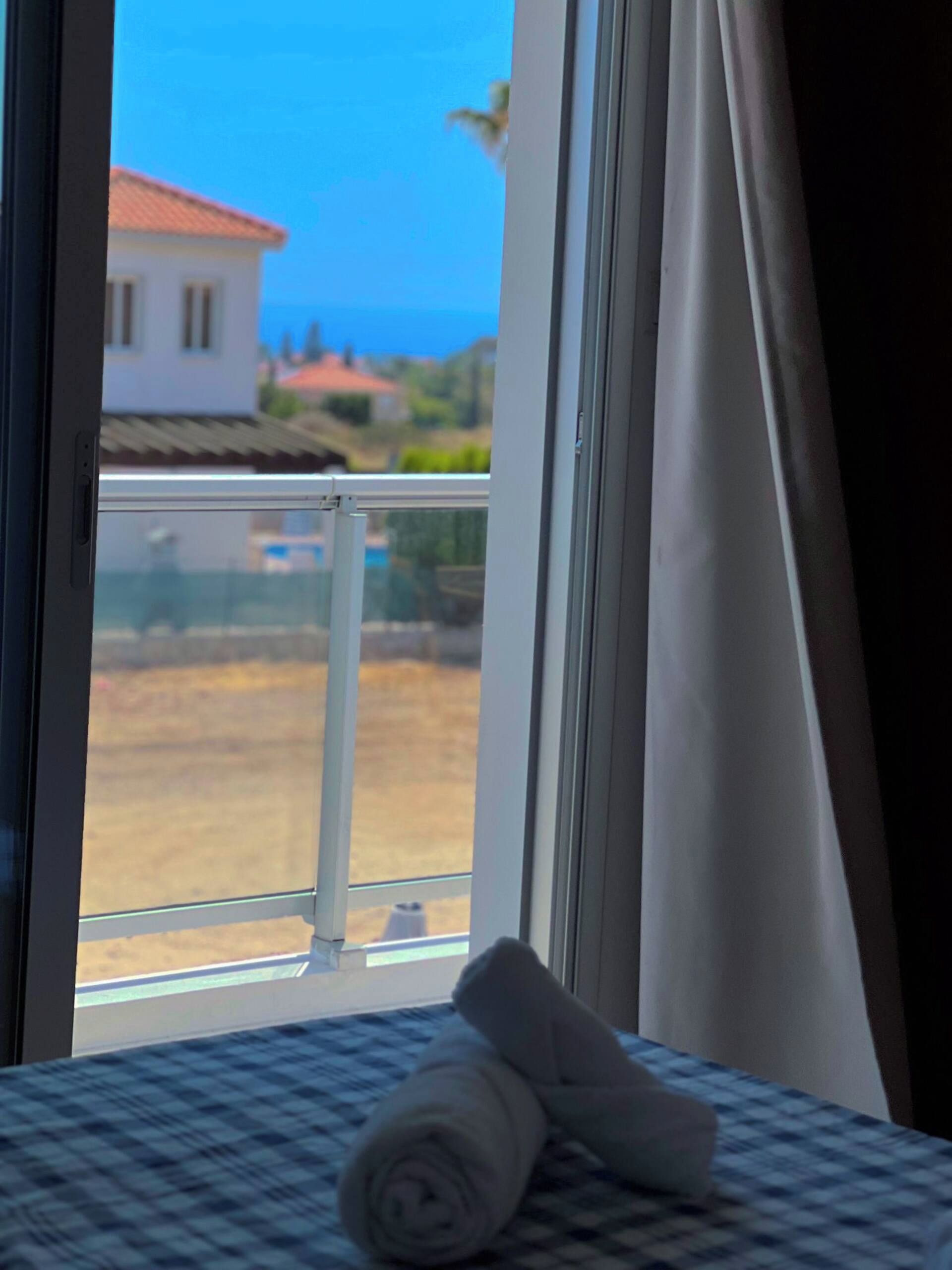 Une chambre d’hôtel avec un lit, une fenêtre avec des rideaux et une vue sur la mer et les bâtiments.