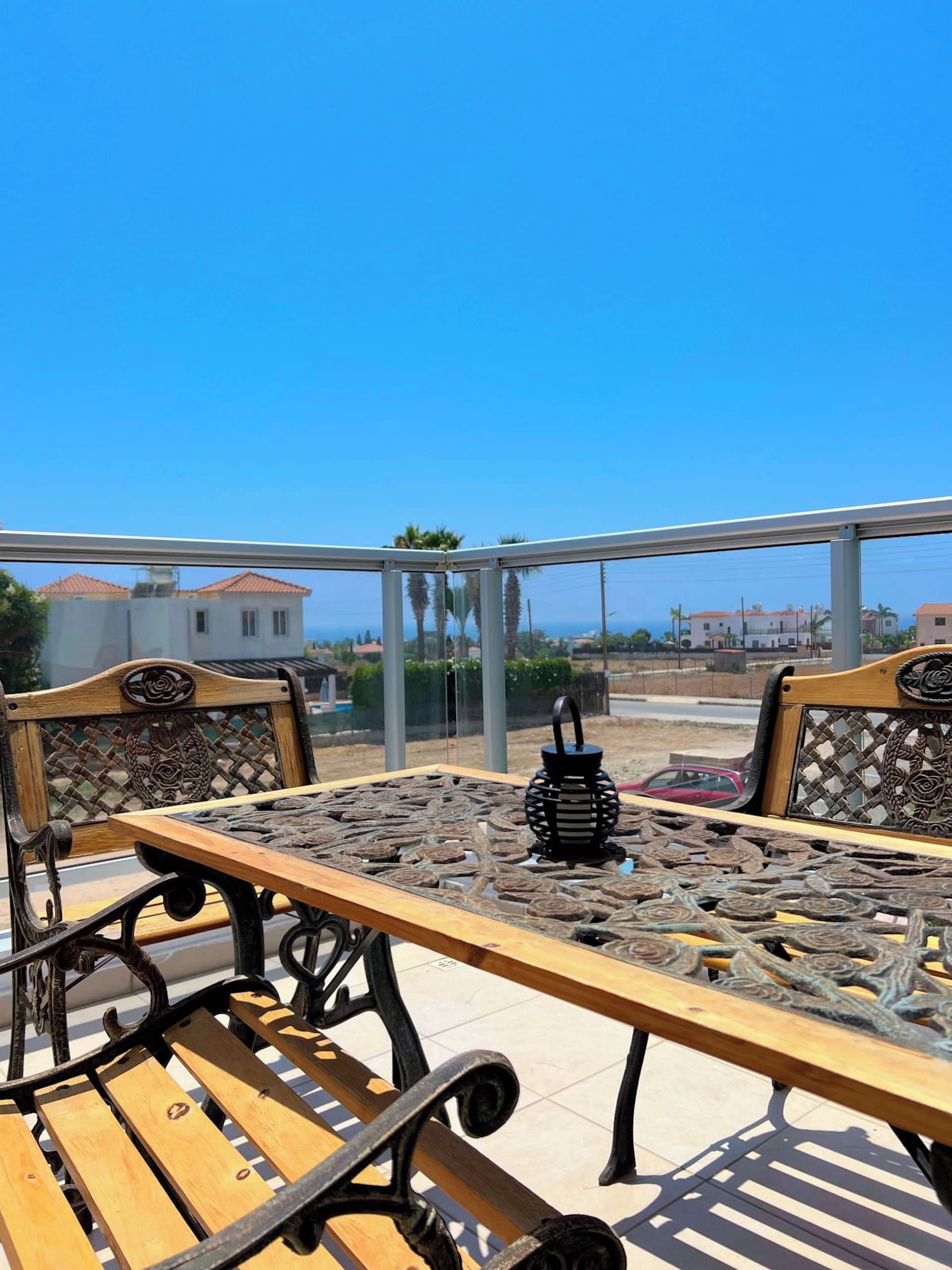 An outdoor seating area with a table and chairs, a decorative lantern, and a view of the sea and buildings.