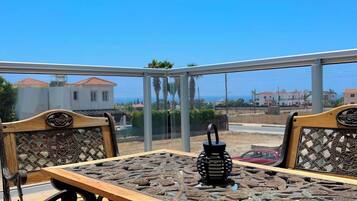 An outdoor seating area with a table and chairs, a decorative lantern, and a view of the sea and buildings.