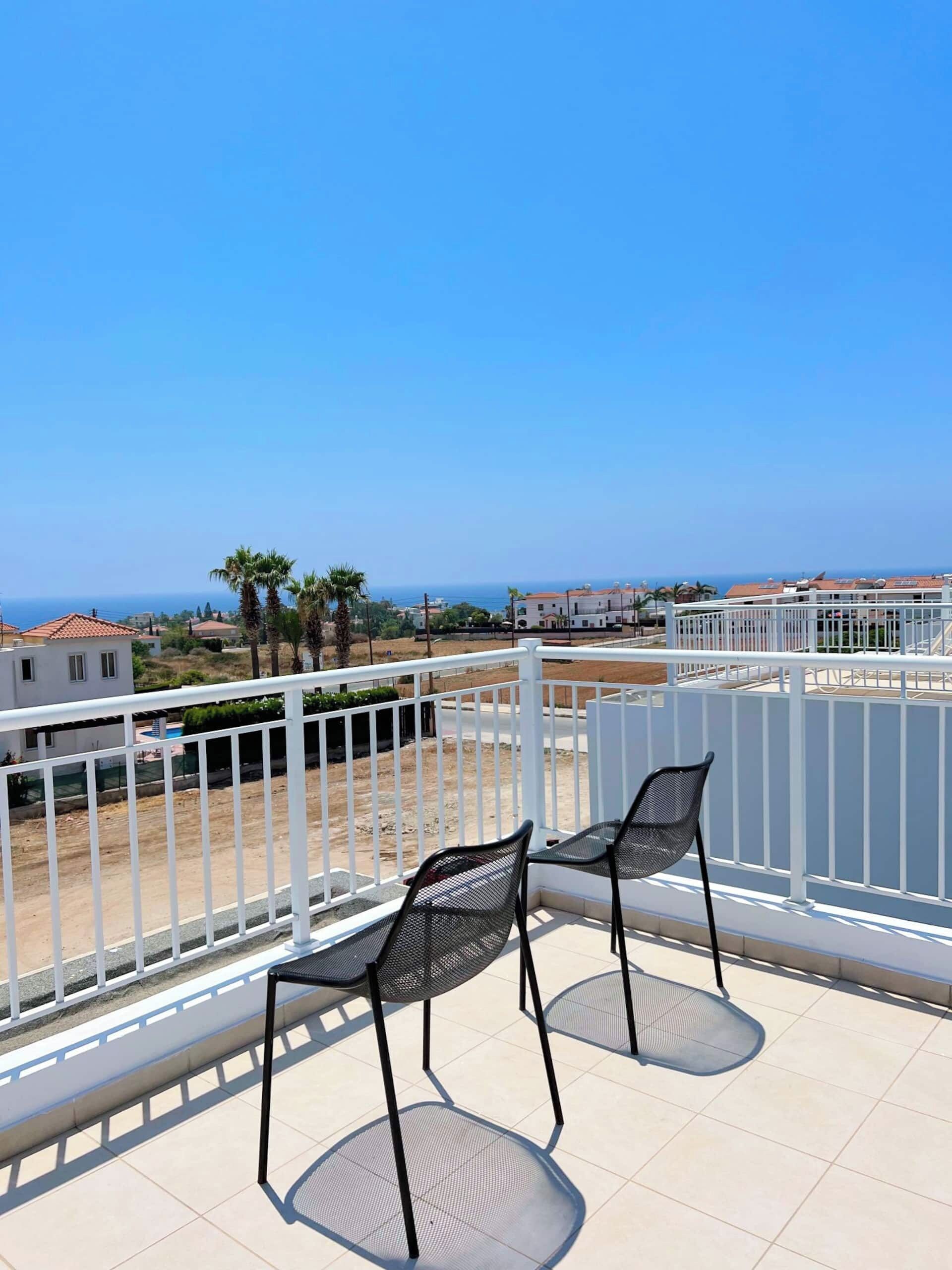 Un balcon avec deux chaises et une vue sur la mer et les bâtiments.