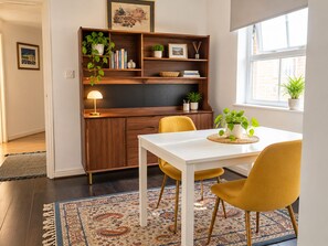 A dining area with a white table, yellow chairs, a wooden bookshelf, and a window with a plant. - Entire 1 bed, zone 2, Peckham, Camberwell, Elephant and Castle (London)