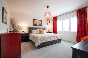 A bedroom with a bed, bedside tables, a lamp, a picture on the wall, and a window with curtains. - Harmony House | Cozy 4-Bedroom Niagara Retreat · EV Charger · Sleeps 8 (Welland)
