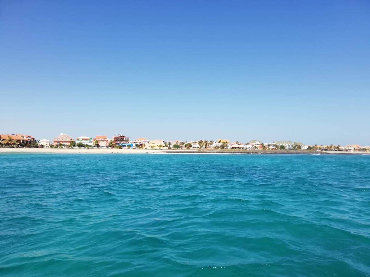 A coastal view with buildings along the shore and calm blue waters.