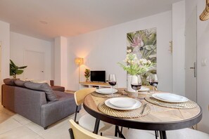 Ein modernes Wohnzimmer mit einem grauen Sofa, einem Esstisch für vier Personen und einem Flachbildfernseher im Hintergrund.