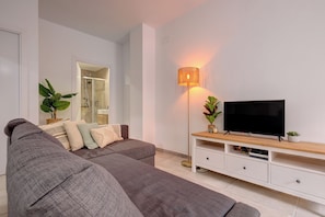 Ein modernes Wohnzimmer mit einem grauen Sofa, einem Flachbildfernseher, einer Stehlampe und einem weißen Schrank.