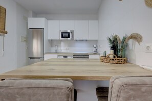 Eine moderne Küche mit weißen Schränken, einem Edelstahl-Kühlschrank, einer Mikrowelle und einem Holzespeisebereich mit zwei gepolsterten Stühlen.