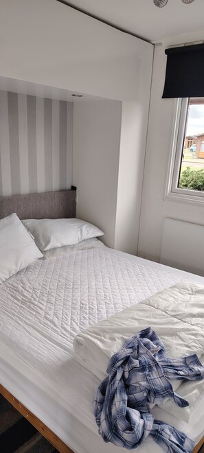 Una cama con un edredón blanco acolchado, almohadas y una camisa de franela azul sobre la misma.