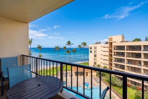 A balcony with a view of the ocean, a pool area, and a building with multiple floors. - Sugar Beach PH08 | Penthouse Ocean Views, Beachfront Pool & Central A/C (Kihei)