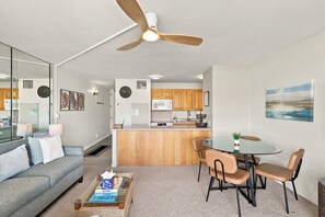 A modern living space with a dining area, kitchen, and a ceiling fan. - Sugar Beach PH08 | Penthouse Ocean Views, Beachfront Pool & Central A/C (Kihei)