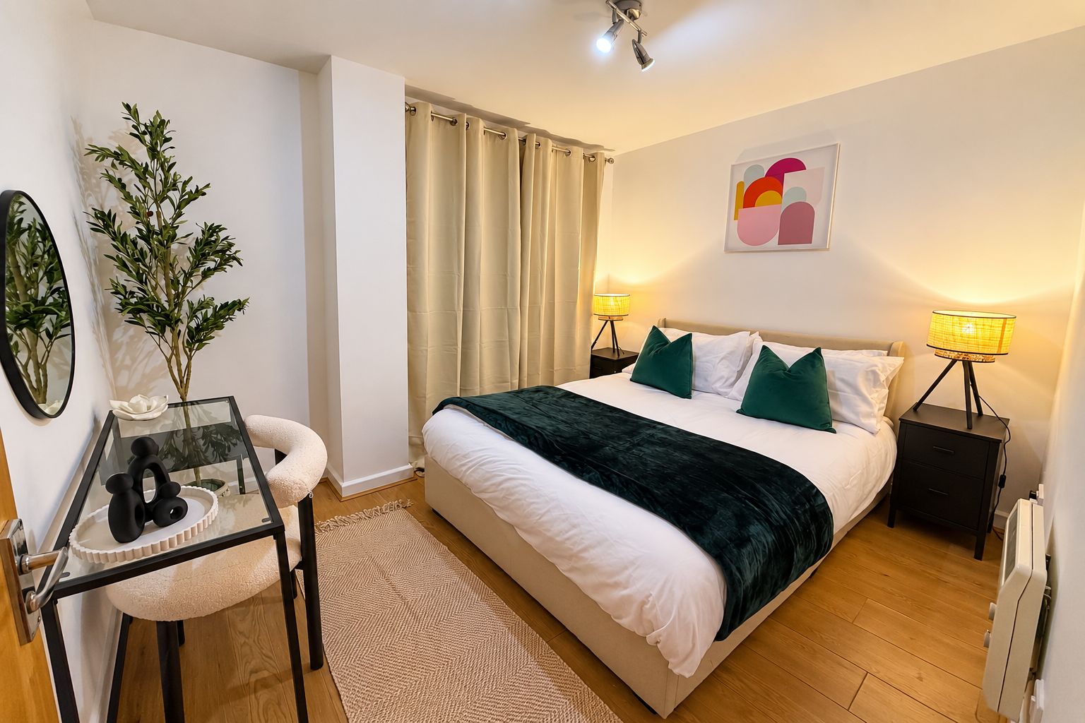 A bedroom with a bed, two bedside tables with lamps, a mirror, a small table with a vase, and a plant.