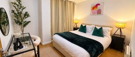 A bedroom with a bed, two bedside tables with lamps, a mirror, a small table with a vase, and a plant.