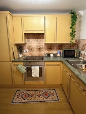A kitchen with wooden cabinets, a microwave, an oven, and a patterned rug. - Luxury 2-Bed 2-Baths City Centre Apartment |  FREE Secure Parking, Balcony (Birmingham)