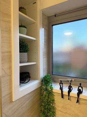 A room with a white shelf unit, a window with frosted glass, and a plant. - Luxury 2-Bed 2-Baths City Centre Apartment |  FREE Secure Parking, Balcony (Birmingham)