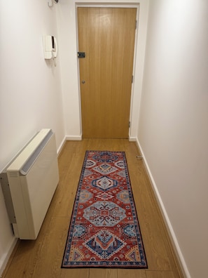 A hallway with a wooden door, a white radiator, and a patterned rug. - Luxury 2-Bed 2-Baths City Centre Apartment |  FREE Secure Parking, Balcony (Birmingham)