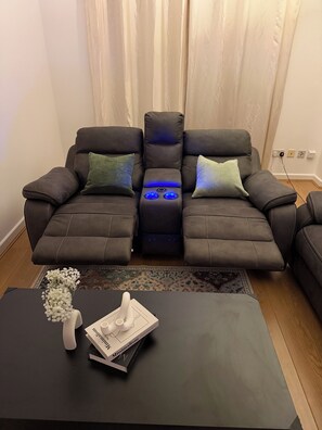 A dark brown leather sofa with blue ambient lighting, a white vase with flowers, and a black coffee table with a book and a tissue box. - Luxury 2-Bed 2-Baths City Centre Apartment |  FREE Secure Parking, Balcony (Birmingham)