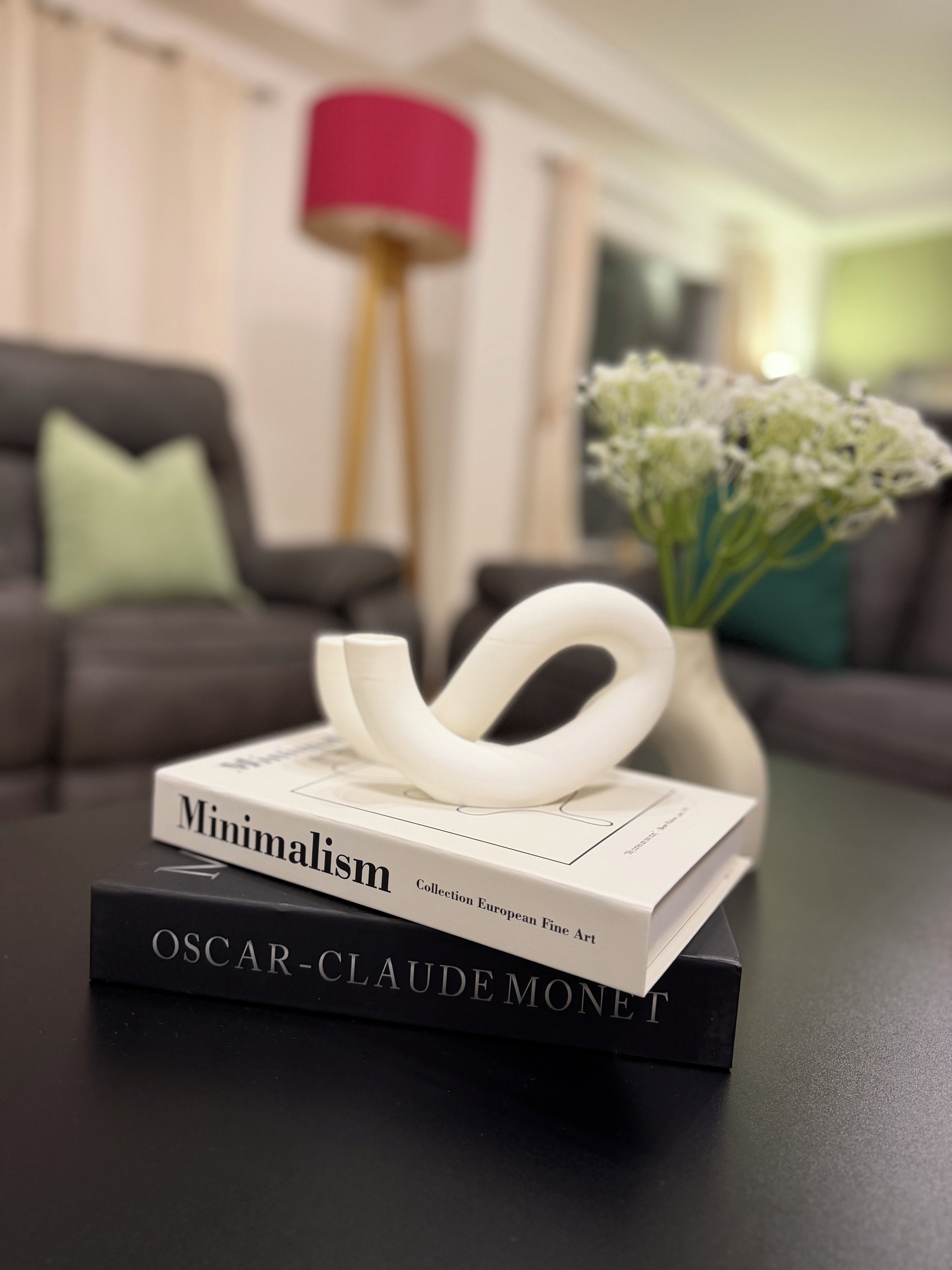 A book titled 'Minimalism' on a table with a vase of flowers and a lamp in the background.